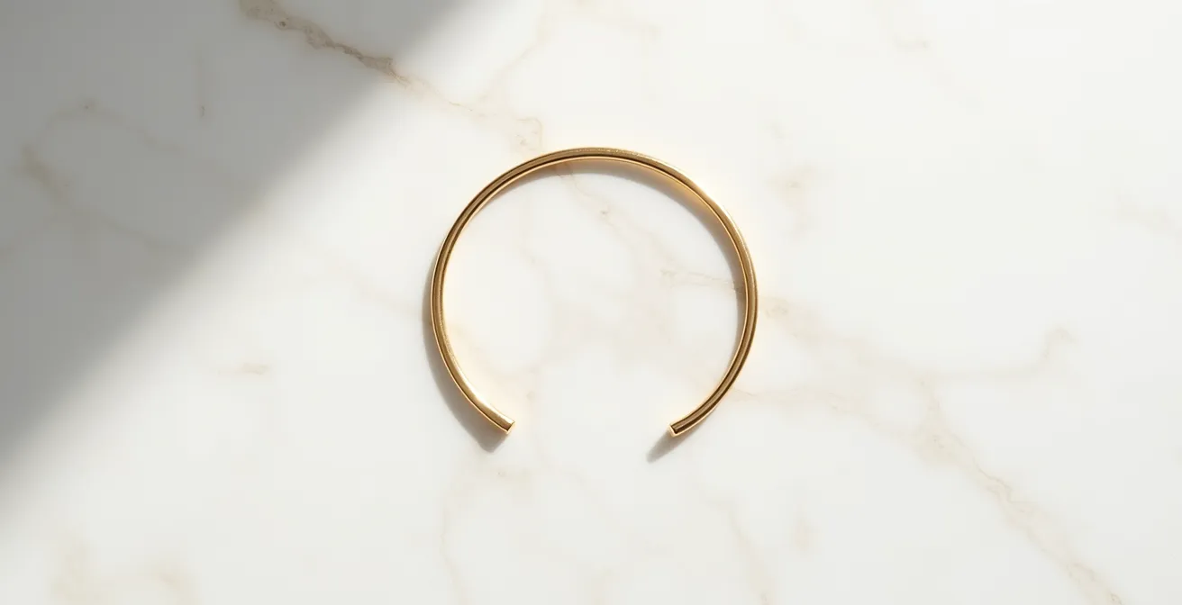Einzelner goldener Armreif auf minimalistischem weissen Hintergrund mit sanftem Schattenwurf